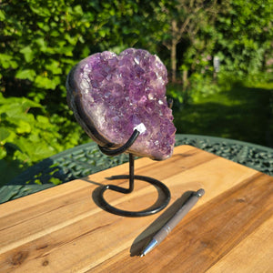 Amethyst Druse Amethyst Geode in Herzform mit Metallsockel 19x16x11cm - NR-36 auf Holzoberfläche mit Stifthalter.
