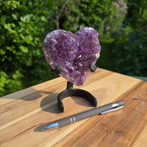 Amethyst Druse Amethyst Geode in Herzform mit Metallsockel 13x9x6cm - NR-50, auf einem Tisch mit einem Stift.