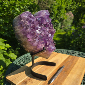 Amethyst Druse Amethyst Geode in Herzform mit Metallsockel 28x24x12cm - NR-14 vor grünem Hintergrund auf Holzunterlage