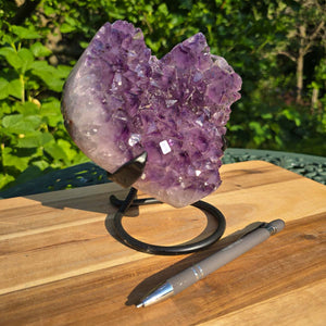 Amethyst Druse Amethyst Geode in Herzform mit Metallsockel 16x15x12cm - NR-33 auf einem Holztisch mit Stift.