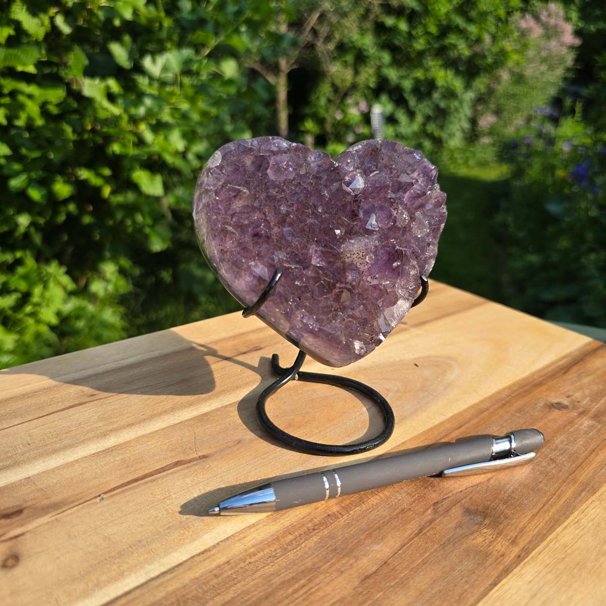 Amethyst Druse Amethyst Geode in Herzform mit Metallsockel 14x11x9cm - NR-53 auf einem Holztisch mit Stift.