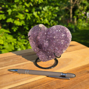 Amethyst Druse Amethyst Geode in Herzform mit Metallsockel 11x11x9cm - NR-47 auf einem Tisch mit Stift.