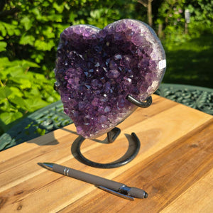 Amethyst Druse Amethyst Geode in Herzform mit Metallsockel 18x16x10cm - NR-43 auf einem Tisch mit Kugelschreiber