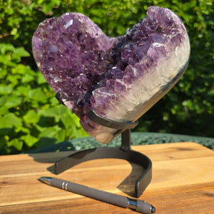 Amethyst Druse Amethyst Geode in Herzform mit Metallsockel 23x20x13cm - NR-19 auf einem stabilen Halter, von Natur umgeben.