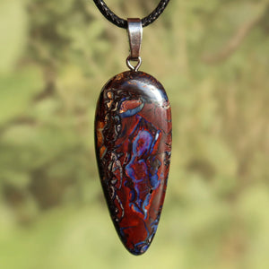 Boulder Opal Anhänger - Positivität und Freude - Nr. 35 mit einzigartigen Mustern auf silberner Öse vor grünem Hintergrund.