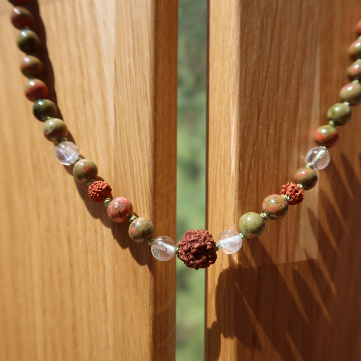 Epidot Unakit, Bergkristall und Rudraksha geknüpfte Kette auf Holzständer, moderne und erdige Naturtöne.