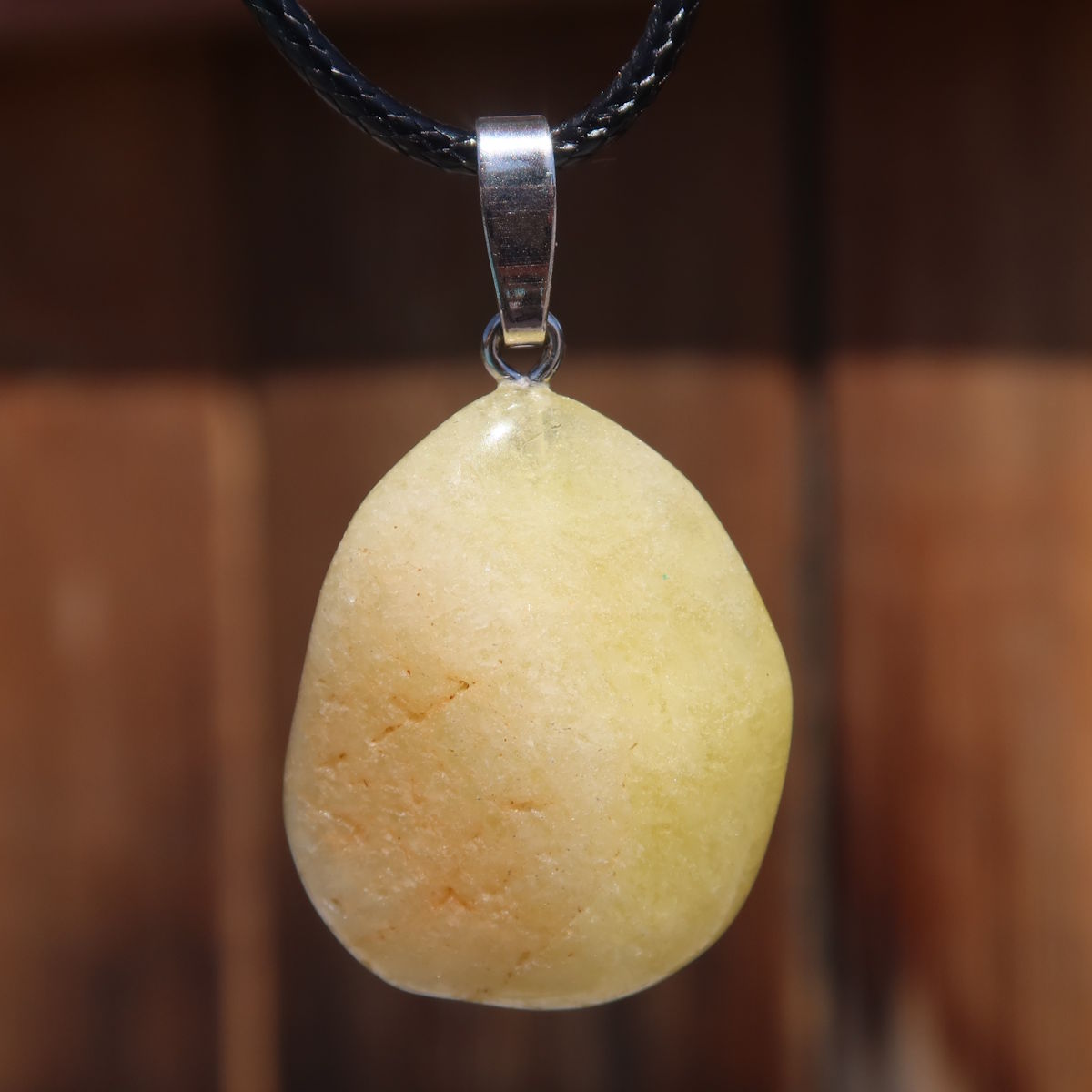 Yellow Danburit pendant in hand, unique gemstone with sunny hue, showcases clear structure and fine color nuances, nature background.