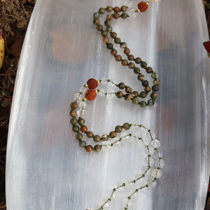 Handgemachte Mala Kette Neubeginn und Klarheit mit Rhyolith, Bergkristall und Rudraksha Perlen auf weißem Hintergrund