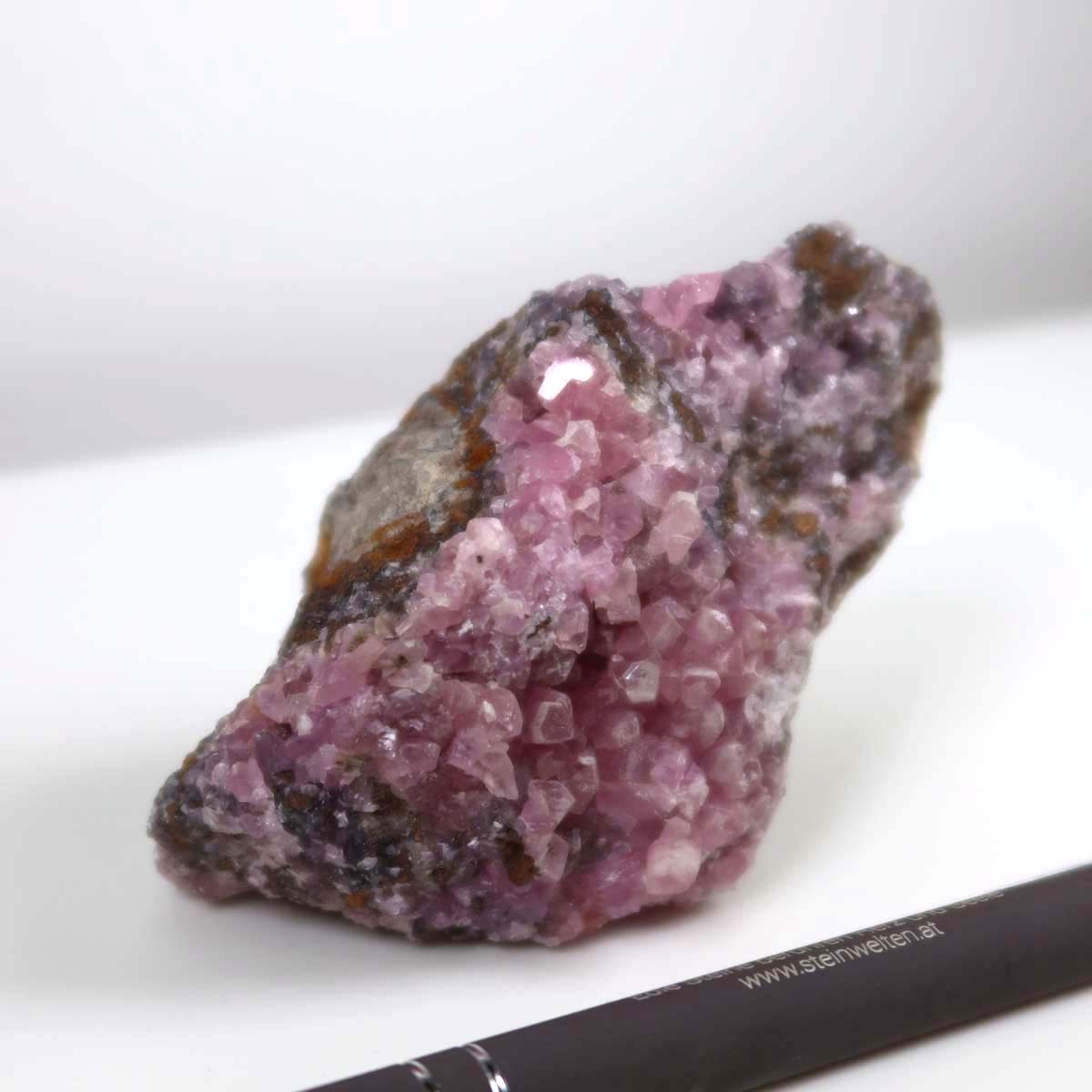 Kobalt Calcit Rohstein in lebendigem Pink mit Kristallstruktur, Rarität aus Marokko, neben einem Stift zur Größendarstellung, 8x6x6 cm.