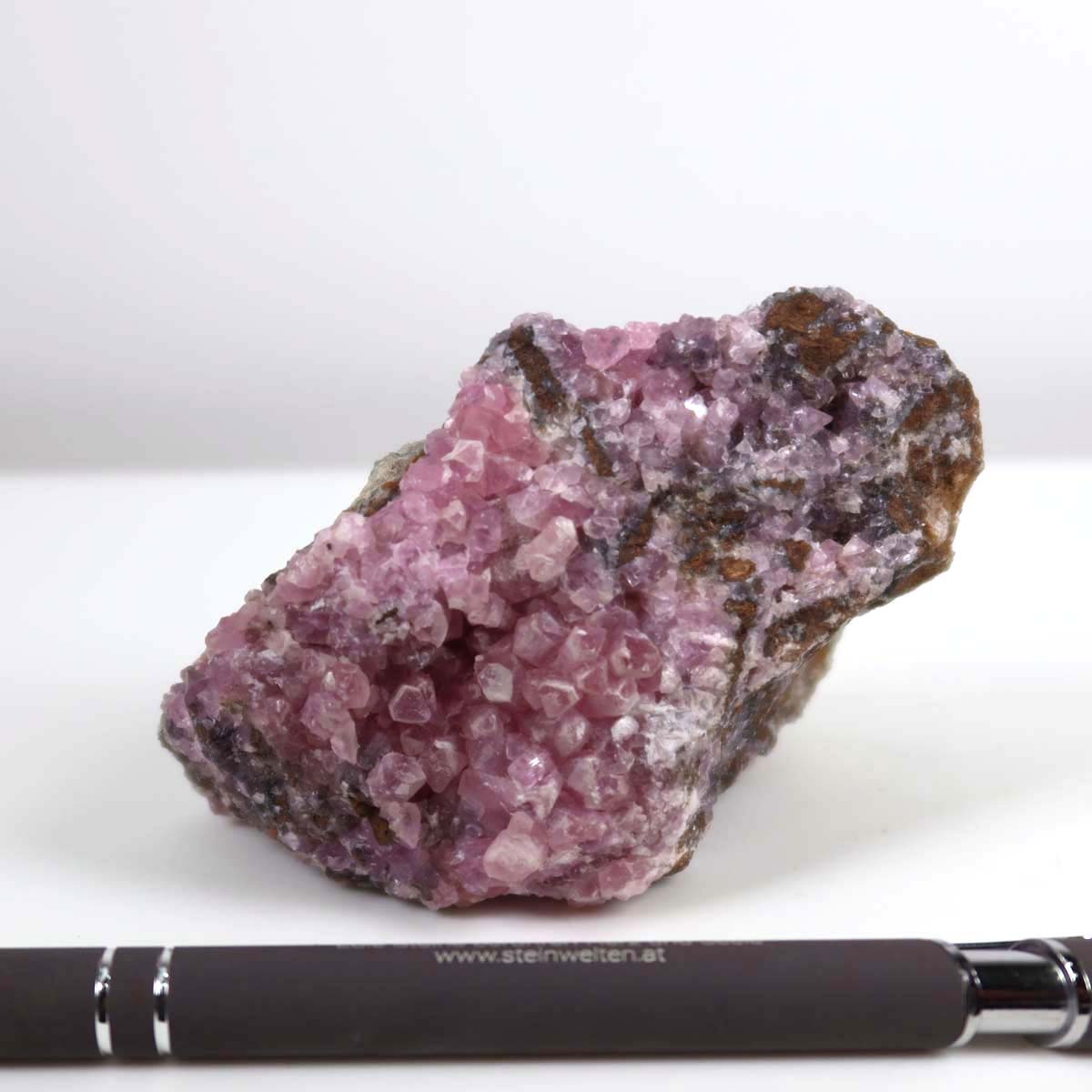 Kobalt Calcit Rohstein in lebendigem Pink mit Kristallstruktur, Rarität aus Marokko, neben einem Stift zur Größendarstellung, 8x6x6 cm.