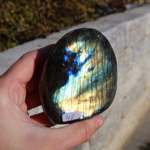 Labradorit Freiform poliert - 7x7cm - Intuition und Kreativität Nr.48 in Hand, mit blauem und goldenem Schimmer im Sonnenlicht.