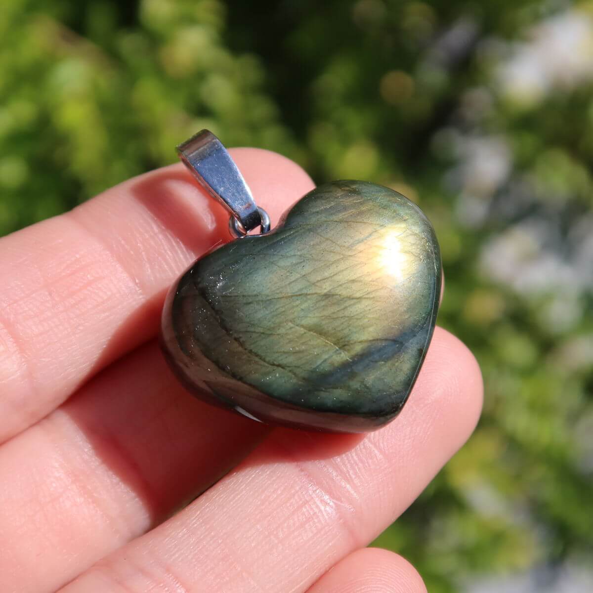 Labradorite heart pendant showing vibrant blue and green hues in sunlight, highlighting its unique spiritual qualities, held by a hand.