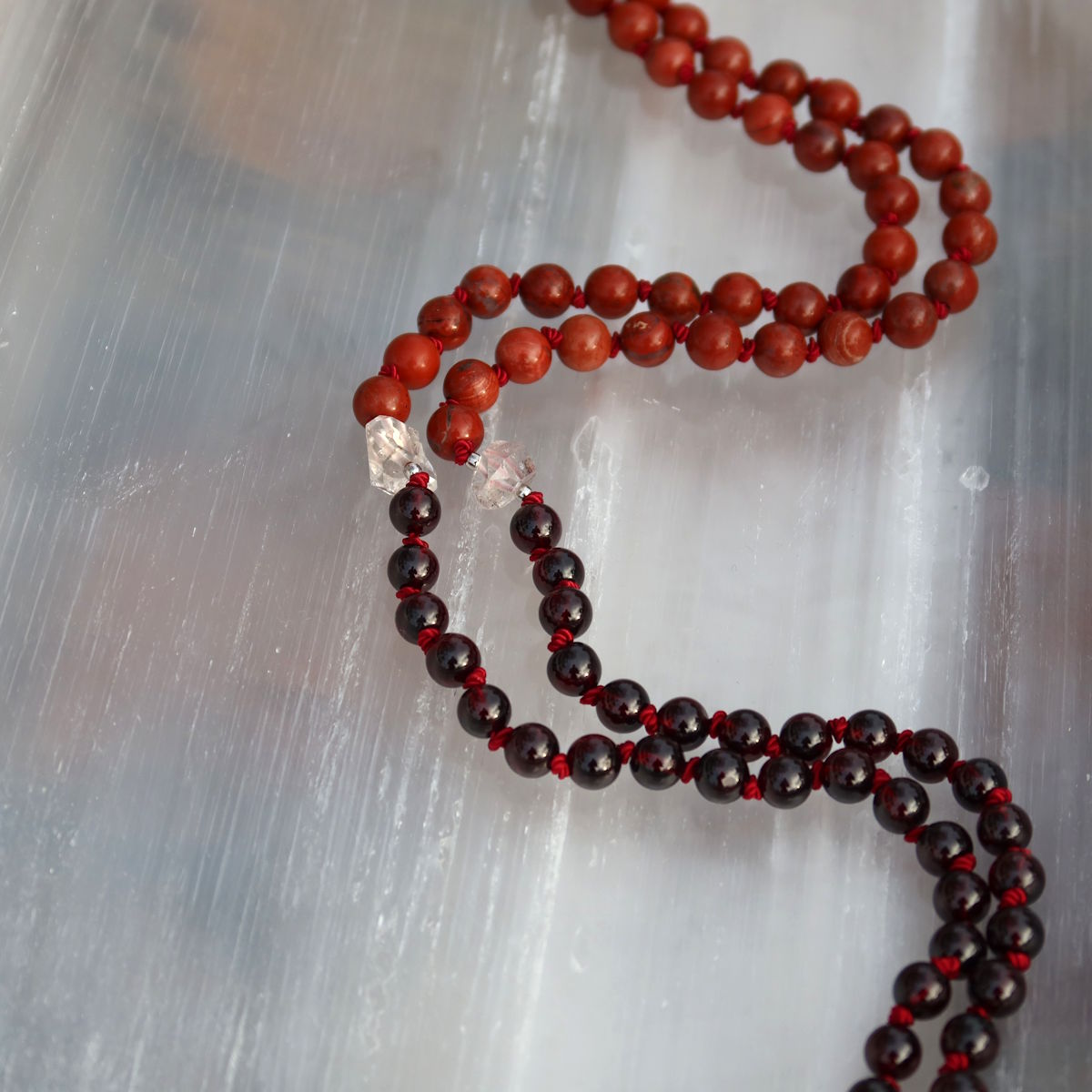 Handgemachte Mala Kette aus Granat und Jaspis auf weißem Teller, symbolisiert Erdung und Stabilität, Kategorie Nr. 24.