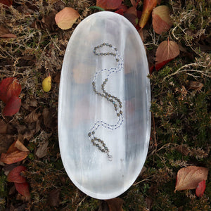 Handgemachte Mala Kette mit Labradorit und Bergkristall, einzigartiges Design, auf natürlichem Hintergrund drapiert.