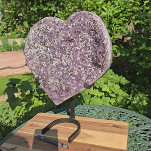 Amethyst Druse Amethyst Geode in Herzform mit Metallsockel 40x34x12cm - NR-26 auf einem Tisch im Garten.