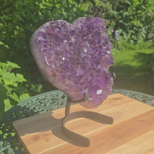 Amethyst Druse Amethyst Geode in Herzform mit Metallsockel 27x20x12cm - NR-4 auf einem Holz Tisch im Garten.