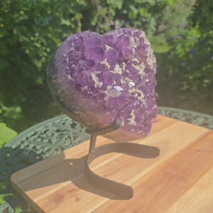 Amethyst Druse Amethyst Geode in Herzform mit Metallsockel 22x20x12cm - NR-6 auf Tisch im Garten.