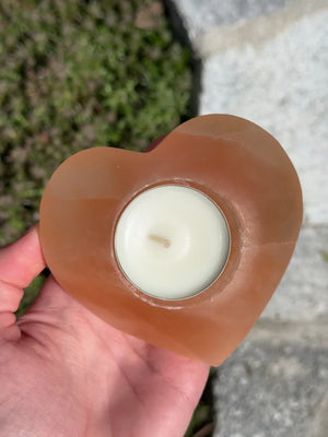 Orange heart-shaped selenite tealight holder, 9cm, known as a light bringer and protective stone, held in hand outdoors.