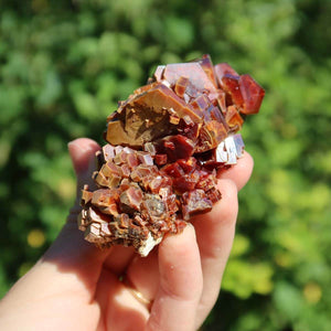 Vanadinit - Natürliche Kristallstufe aus Marokko 7x4,5x4,5cm - 0,22kg Nr.49 in einer Hand mit grünem Hintergrund.