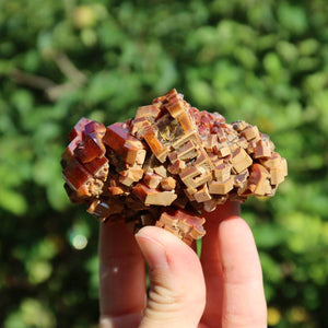 Vanadinit - Natürliche Kristallstufe aus Marokko 7x4,5x4,5cm - 0,22kg Nr.49 in der Hand, vor grünem Hintergrund.